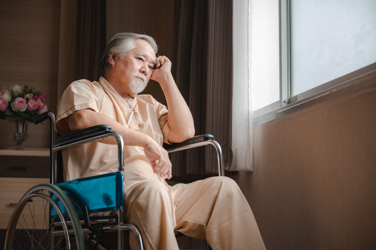 Senior male patient with grey hair and hospital clothing sitting on wheelchair